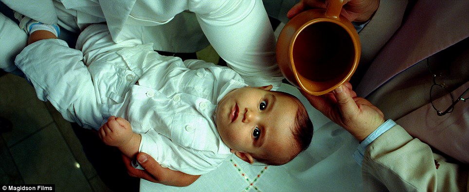 Healing waters: An infant looks up at the camera before he gets baptized
