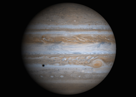 A full face of Jupiter with the Great Red Spot on the right hand side. A small dark spot on the left side of Jupiter is the shadow of a moon passing in front.