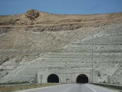 Photo shows view from a highway looking at two arched tunnel entrances into the rock face of a mountain.