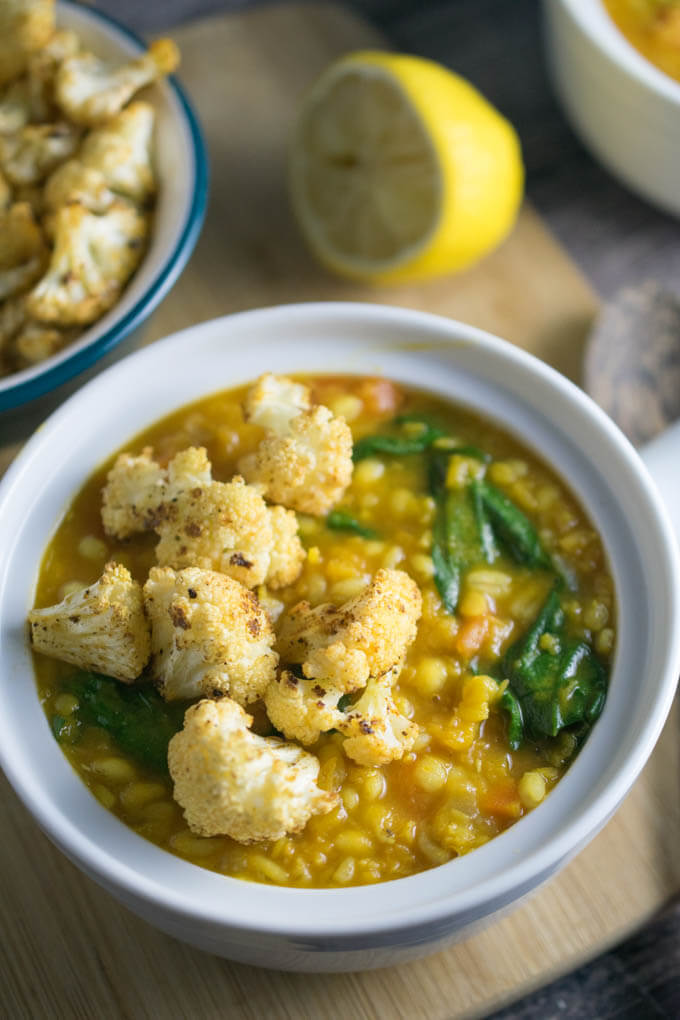 Baked and blackened cauliflower bites topping a hearty golden lentil vegan soup swirled with lemon juice and wilted spinach greens