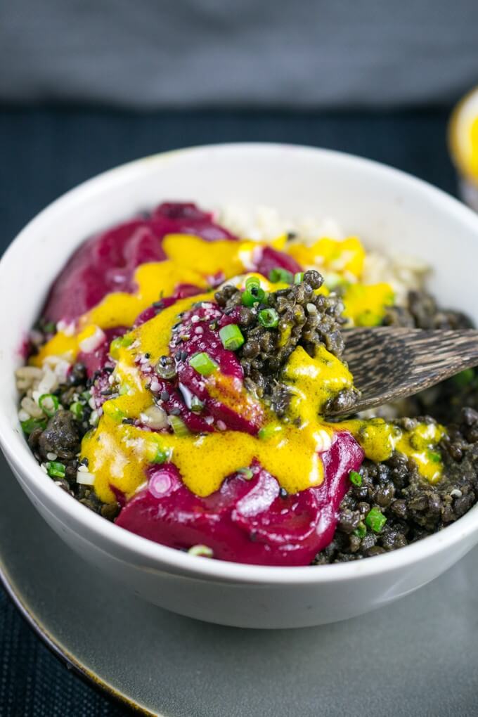 A bowl of Peruvian black lentils, beetroot sauce, and bright yellow aji amarillo chili oil drizzled over the top